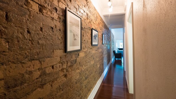 A hallway with a brick wall and framed pictures. - Hampton Court Apartments (Clayfield)