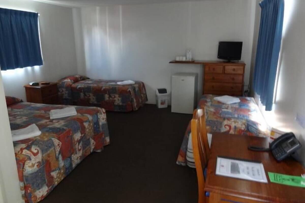 Une chambre d’hôtel avec deux lits, un bureau avec un téléphone, un petit réfrigérateur et un téléviseur posé sur une commode.
