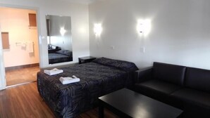 A modern hotel room with a bed, a sofa, a small table, and a mirror. - Jolly Collier Hotel Motel (Dysart)