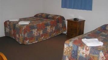 Une chambre avec deux lits, chacun recouvert d’une couvre-lit aux motifs colorés. Une table de chevet en bois se trouve entre les lits, et un rideau bleu est accroché au mur.
