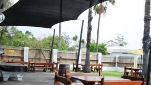 An outdoor patio area with wooden tables and benches, surrounded by a black canopy. - Jolly Collier Hotel Motel (Dysart)