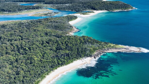 An aerial view of a coastal area with a beach, clear blue waters, and dense forested hills. - Jackson Ranch by Bannisters (Bawley Point)