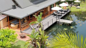 A modern house with a large deck overlooking a pond, surrounded by dense forest. - Jackson Ranch by Bannisters (Bawley Point)