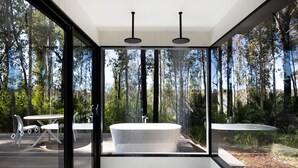 A modern outdoor bathroom with a freestanding bathtub, a glass-enclosed shower area, and a dining table with chairs. - Jackson Ranch by Bannisters (Bawley Point)