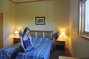 Un dormitorio con cama, dos mesitas de noche con lámparas, un cuadro enmarcado en la pared y una ventana.