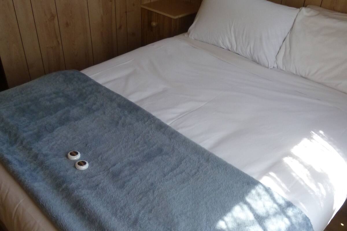 Een kamer met houten lambrisering, een bed, nachtkastje en raam met gordijnen.