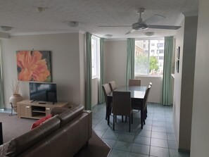 A living room with a sofa, TV, and a dining area with a table and chairs. - The Bay Apartments (Coolangatta)