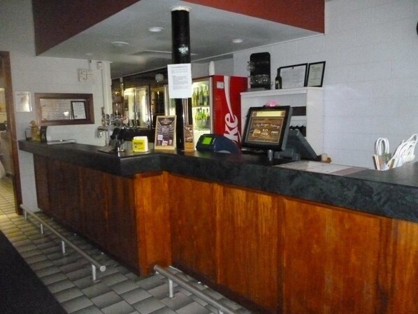 A reception area with a wooden counter, a Coca-Cola refrigerator, a digital display, and a framed certificate on the wall.