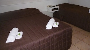 Une chambre d’hôtel avec deux lits, chacun recouvert d’une couverture marron et agrémenté de serviettes blanches soigneusement pliées.