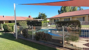 A fenced backyard with a swimming pool, a covered patio, and a house with a red roof.