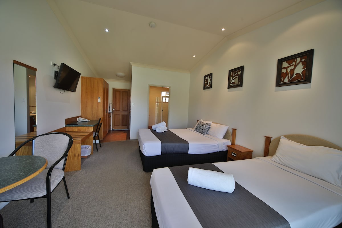 A hotel room with two beds, a desk, a chair, and a television.