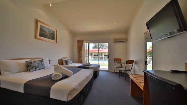 A hotel room with two beds, a TV, a desk, and a view of the outside.