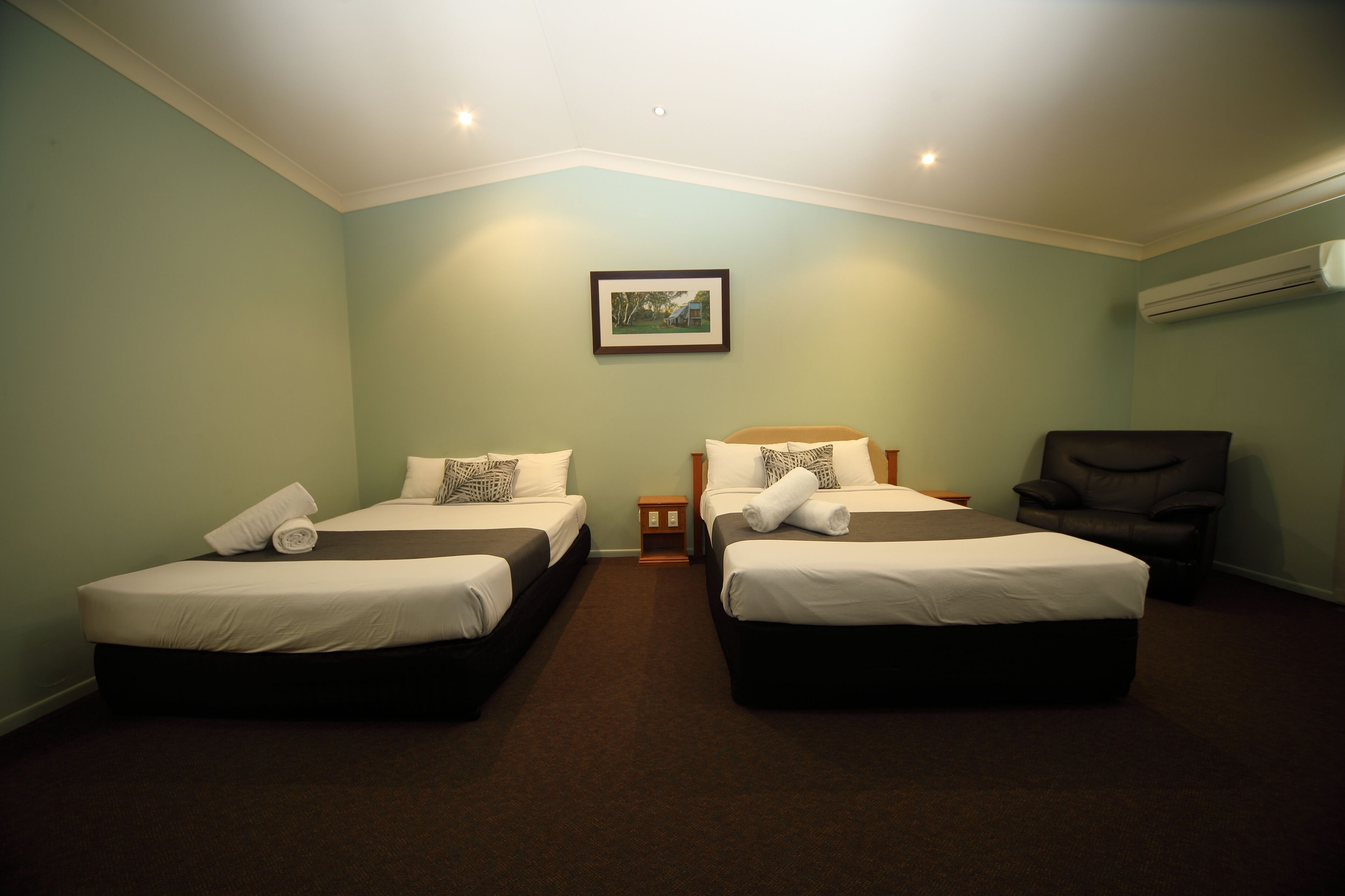 Habitación de hotel con dos camas, una mesita, una silla y un cuadro en la pared.