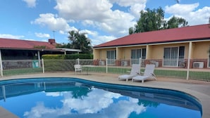 A swimming pool with lounge chairs, a fenced area, and a building with a red roof.