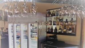 A bar area with a refrigerator stocked with beverages, shelves with bottles, and hanging wine glasses.