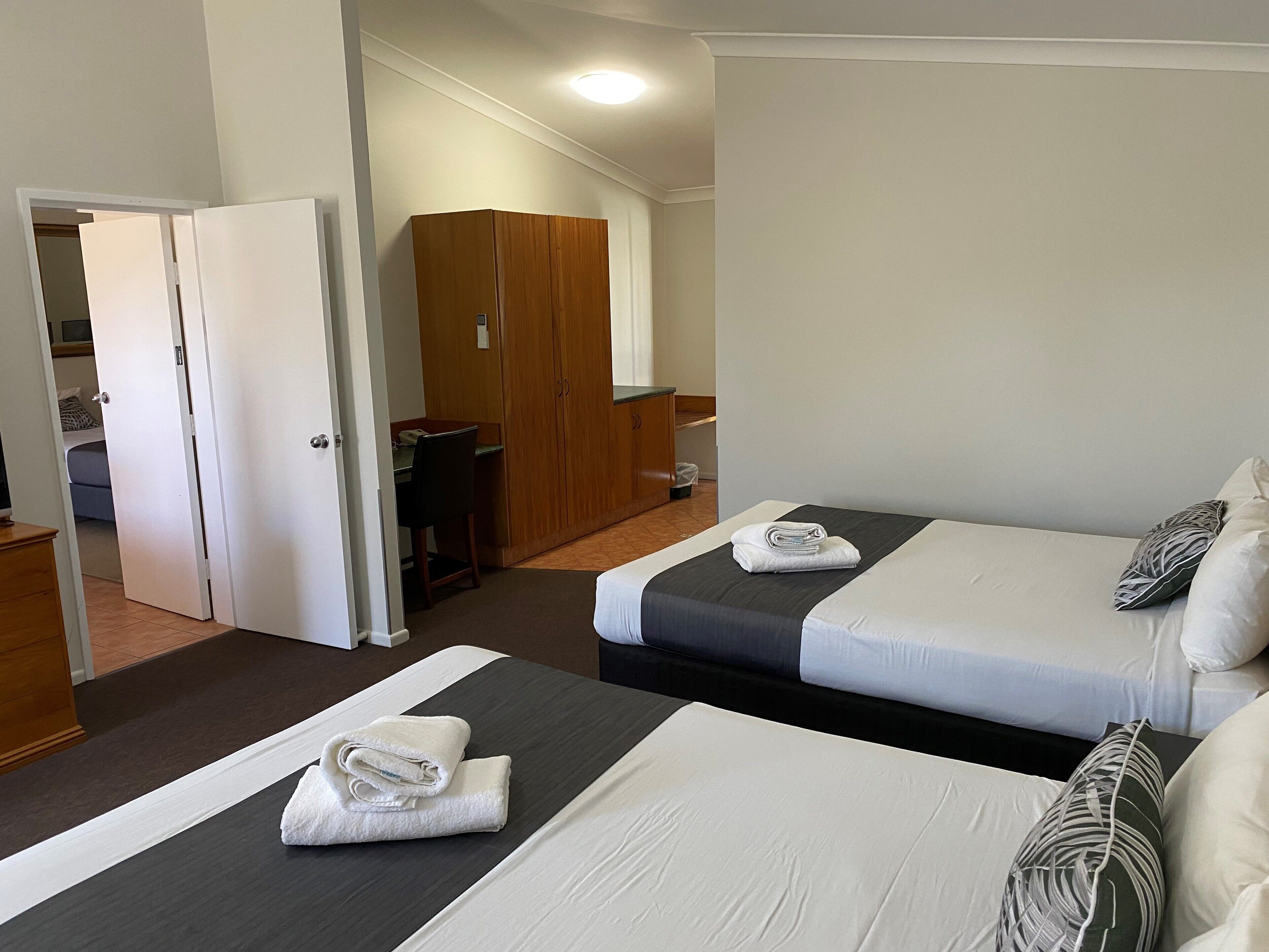 Una habitación de hotel con dos camas, un armario, un escritorio y un baño.