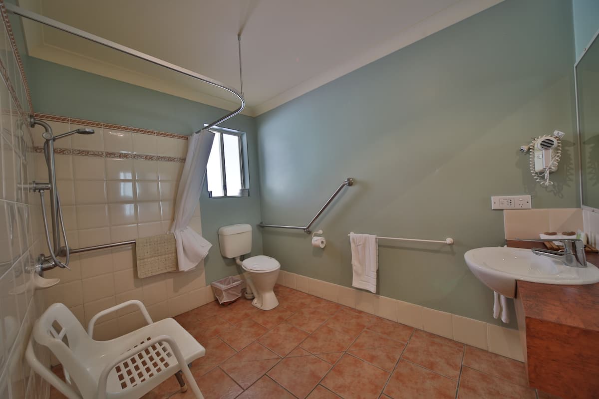A bathroom with a toilet, sink, shower, and grab bars.