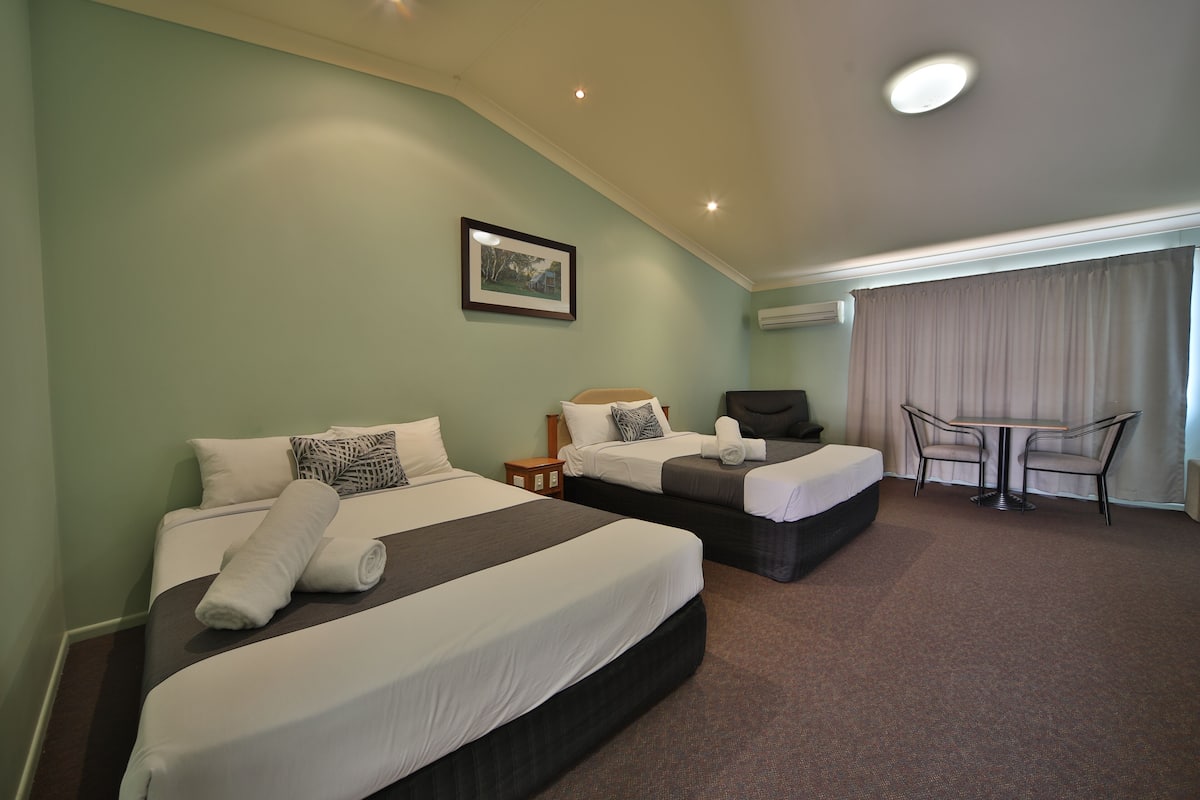 A hotel room with two beds, a small table, and a chair.
