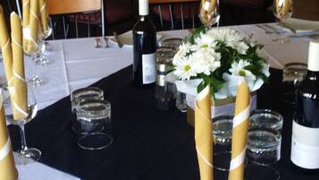 A banquet hall with tables set for a formal event, featuring white tablecloths, gold napkin holders, and floral centerpieces.