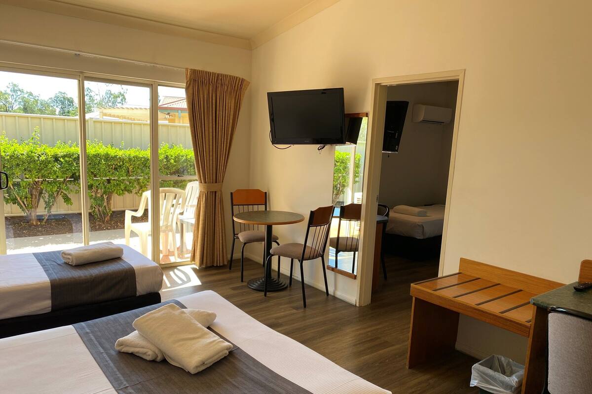 A hotel room with two beds, a TV, a dining table, and a small desk.