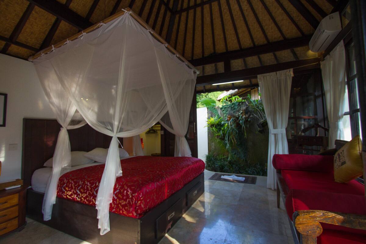 A room with a bed under a canopy, a red sofa, and a small table.