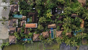 Eine Vogelperspektive zeigt ein Resort mit mehreren Bungalows, Schwimmbecken und üppiger tropischer Vegetation.