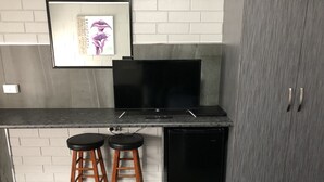 A kitchen with a black countertop, two wooden stools, a black dishwasher, and a framed picture on the wall. - Mariner Motel (Portland)