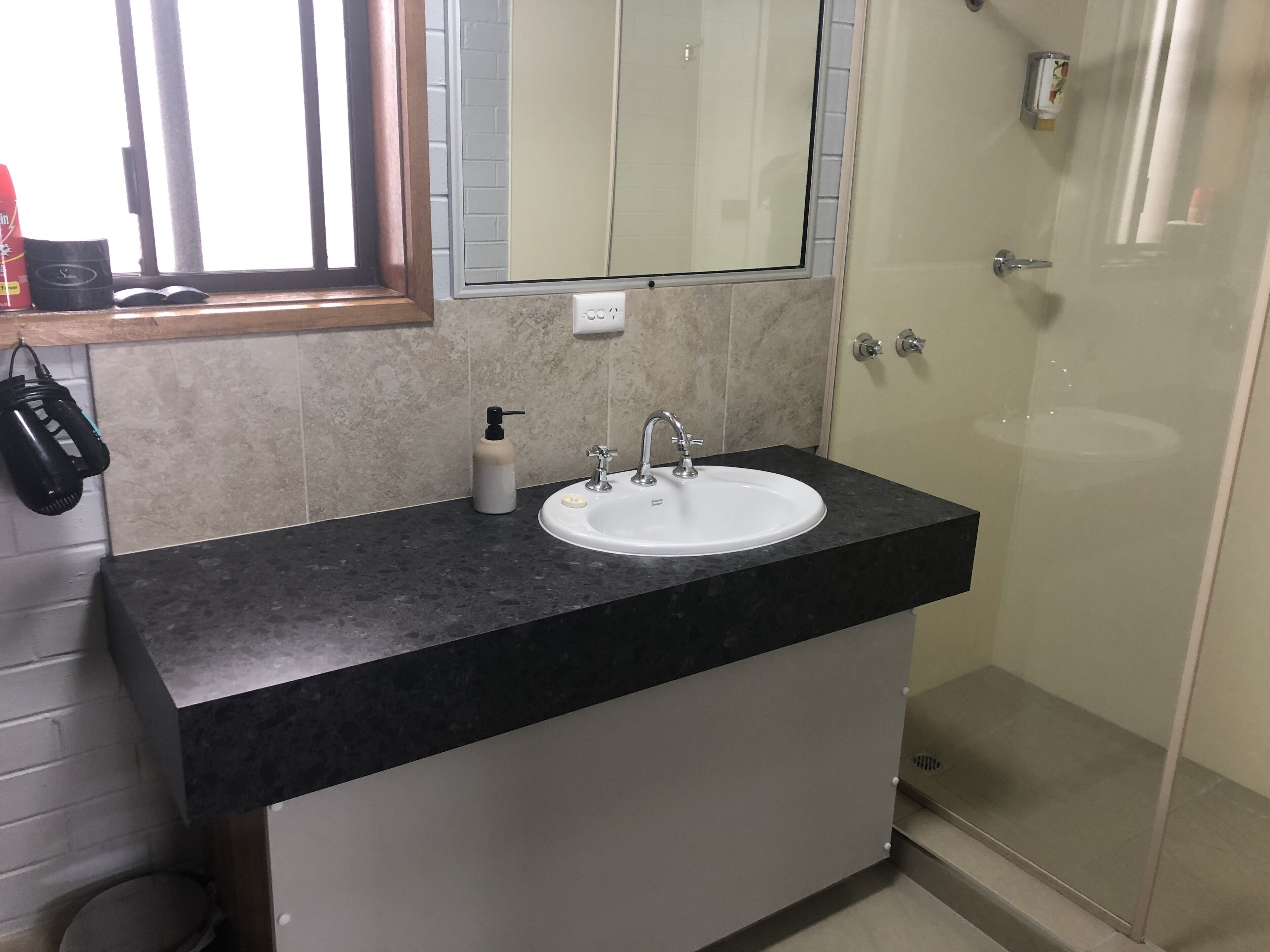 Uma casa de banho com bancada preta, lavatório branco, espelho e chuveiro.