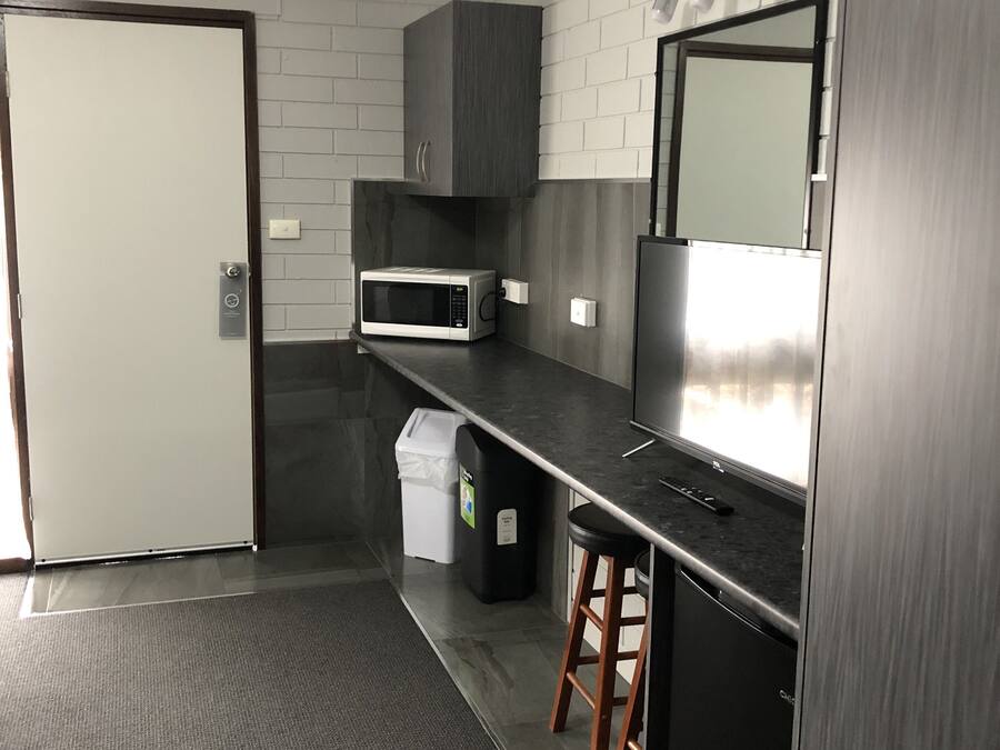A modern kitchen with grey brick walls, a stainless steel refrigerator, a microwave, and a small trash bin.