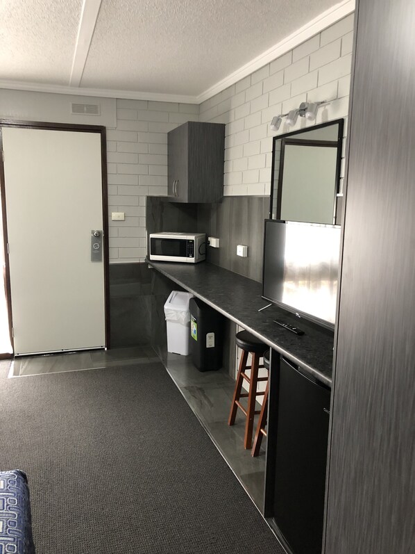 Una cocina moderna con paredes de ladrillo gris, un refrigerador de acero inoxidable, un microondas y un pequeño cubo de basura.