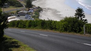 A coastal road with a beach on one side and a parking area with several cars. - Mariner Motel (Portland)