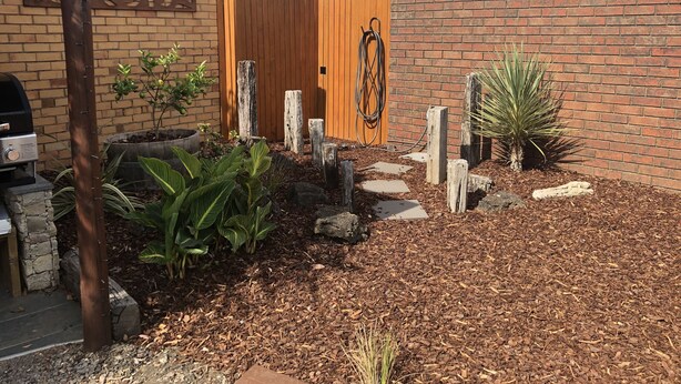 A garden area with a brick wall, wooden fence, and various plants. - Mariner Motel (Portland)