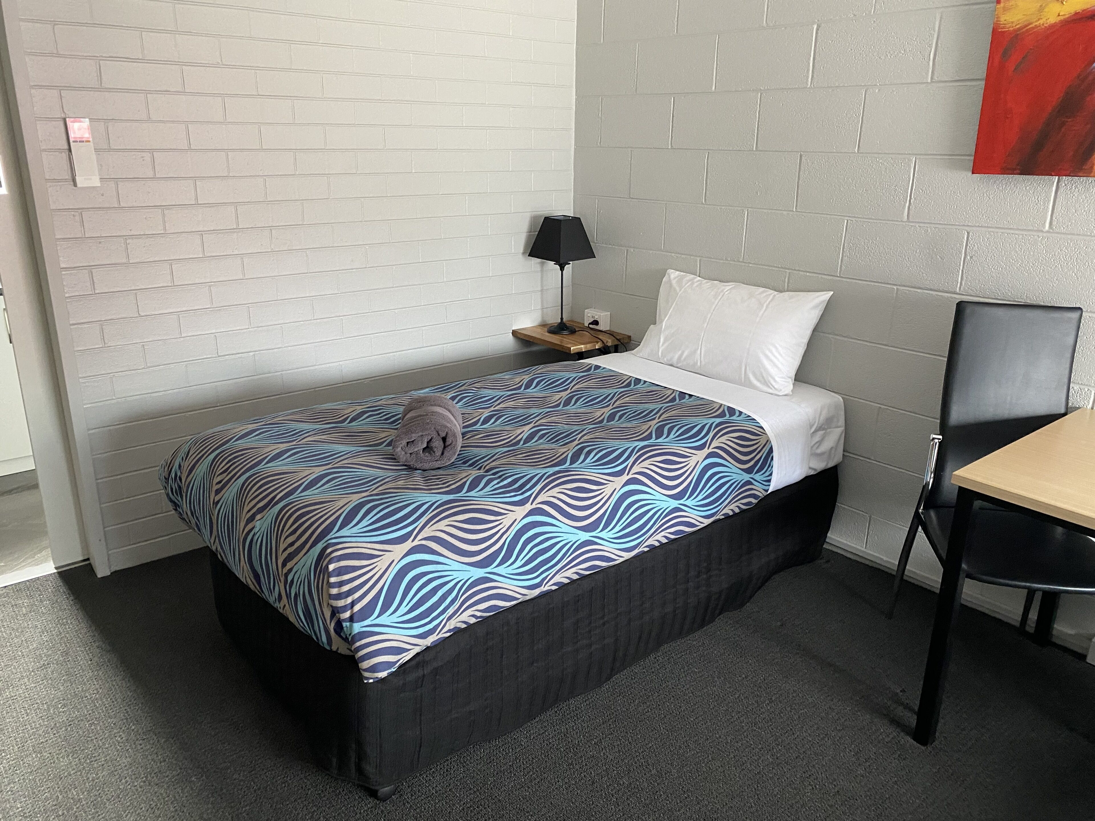 A hotel room with a bed, a nightstand, a lamp, a chair, and a painting on the wall.