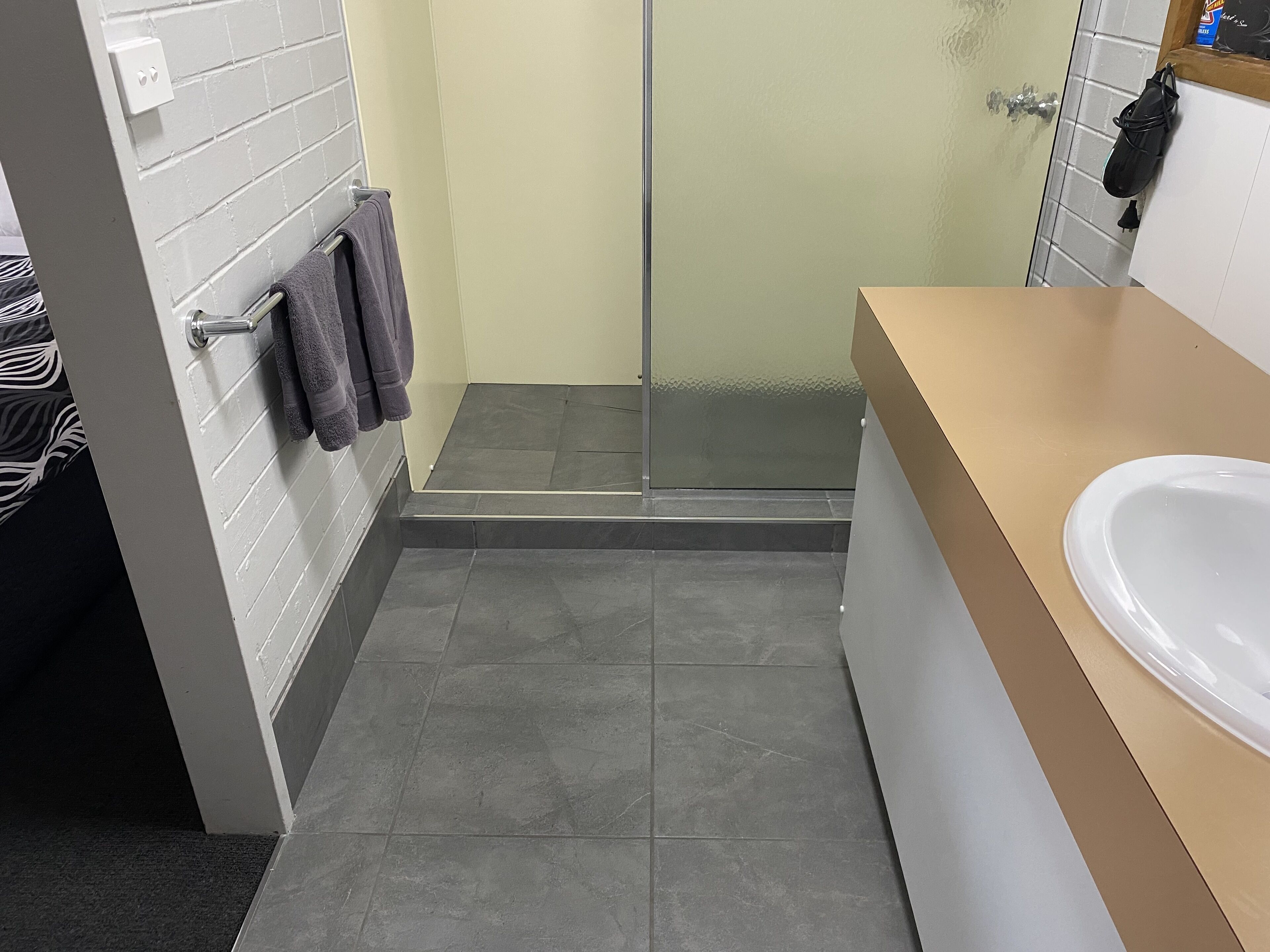 Un baño con ducha, lavamanos y un perchero para toallas.