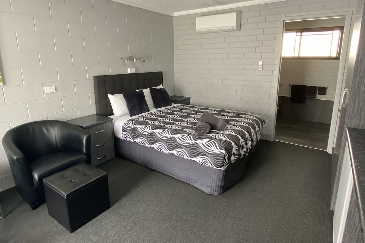 A bedroom with a bed, a chair, a nightstand, a small table, and a bathroom door.