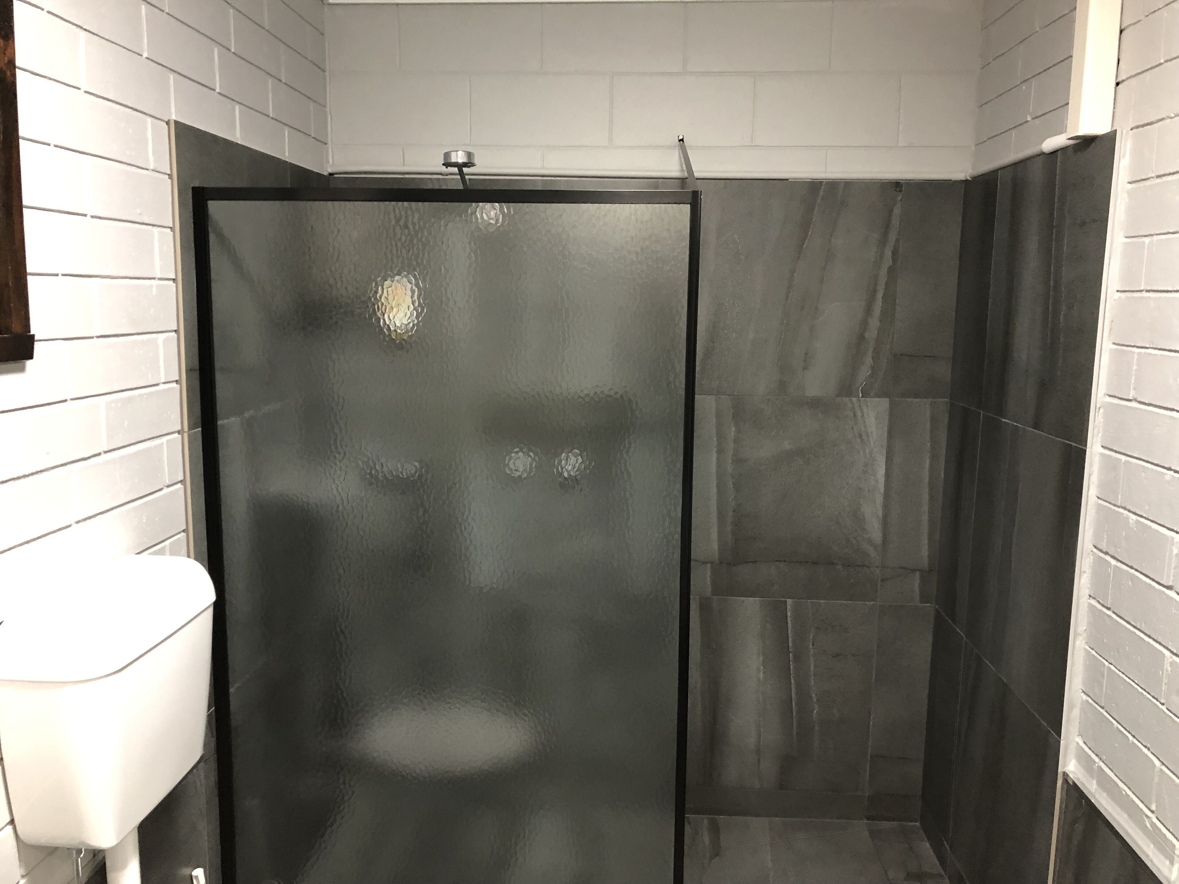 Un bagno con cabina doccia in vetro, pareti piastrellate di bianco e un water bianco.