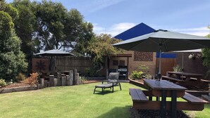 A backyard with a barbecue area, picnic tables, and a wooden deck. - Mariner Motel (Portland)