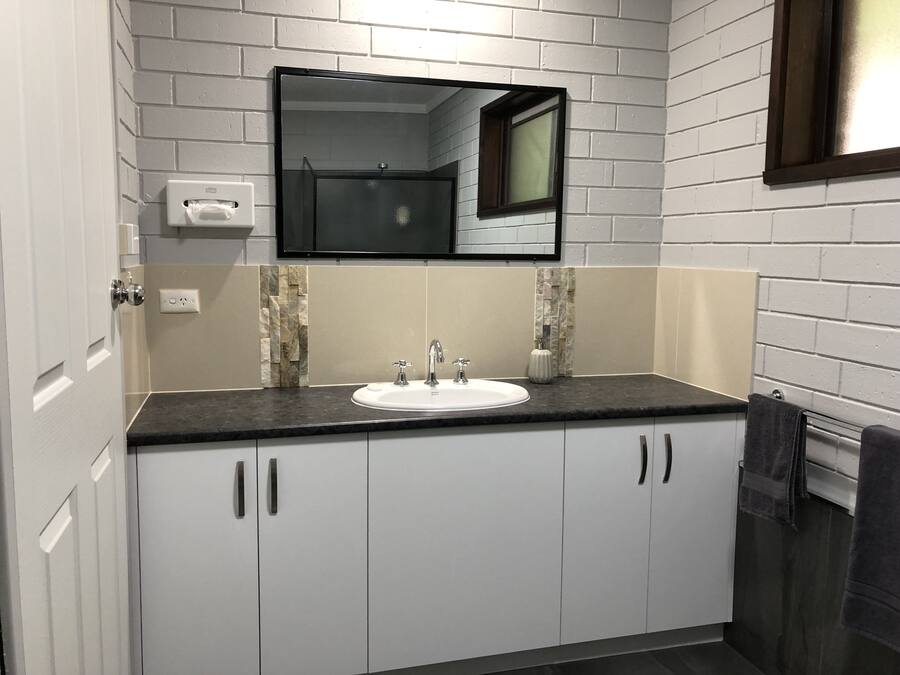 Un baño moderno con un lavabo blanco, encimera oscura y un espejo sobre el lavabo.