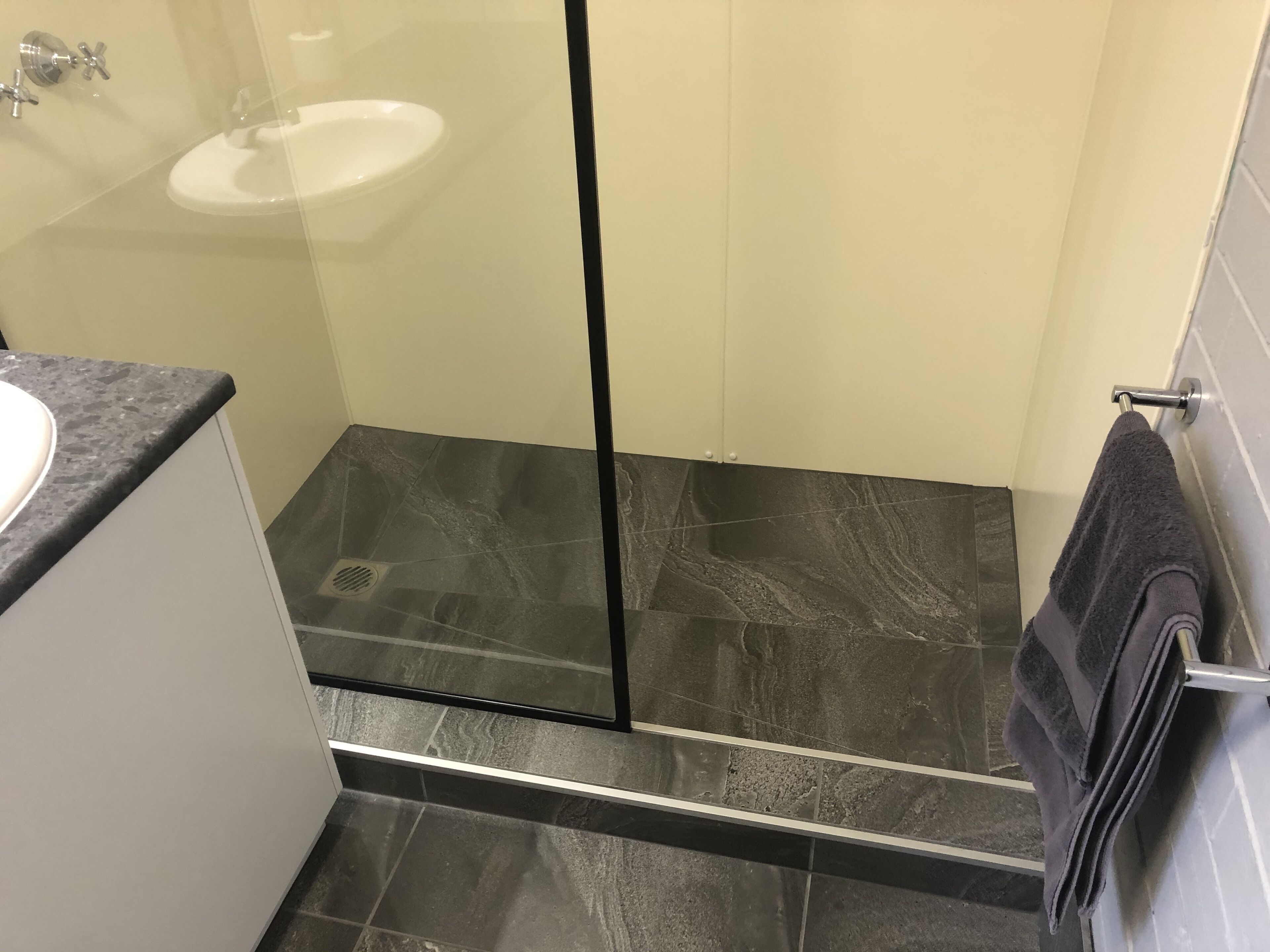 Um banheiro moderno com box de vidro, pia branca e piso com azulejos escuros.