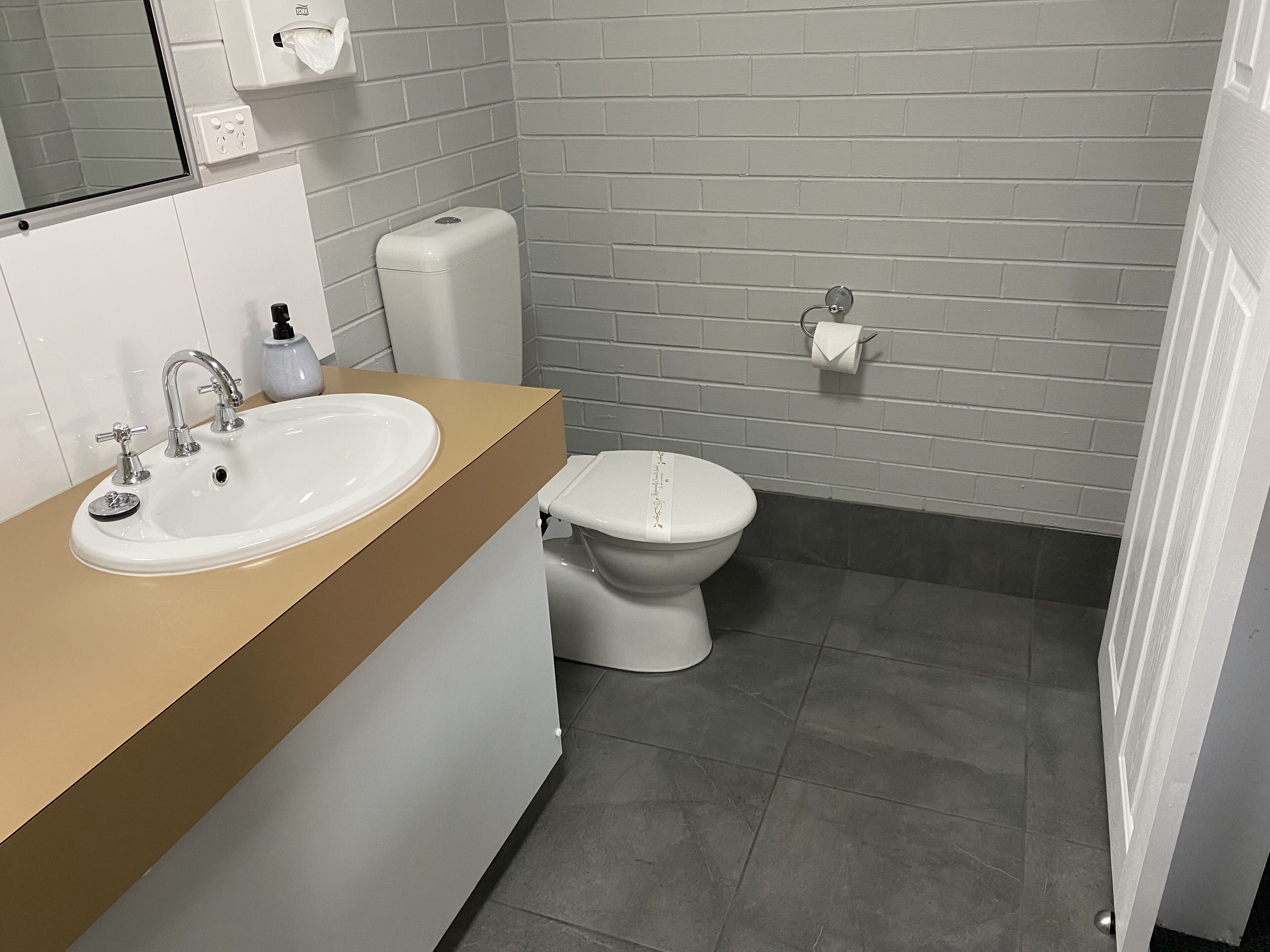 A bathroom with a white sink, a toilet, and a towel dispenser.