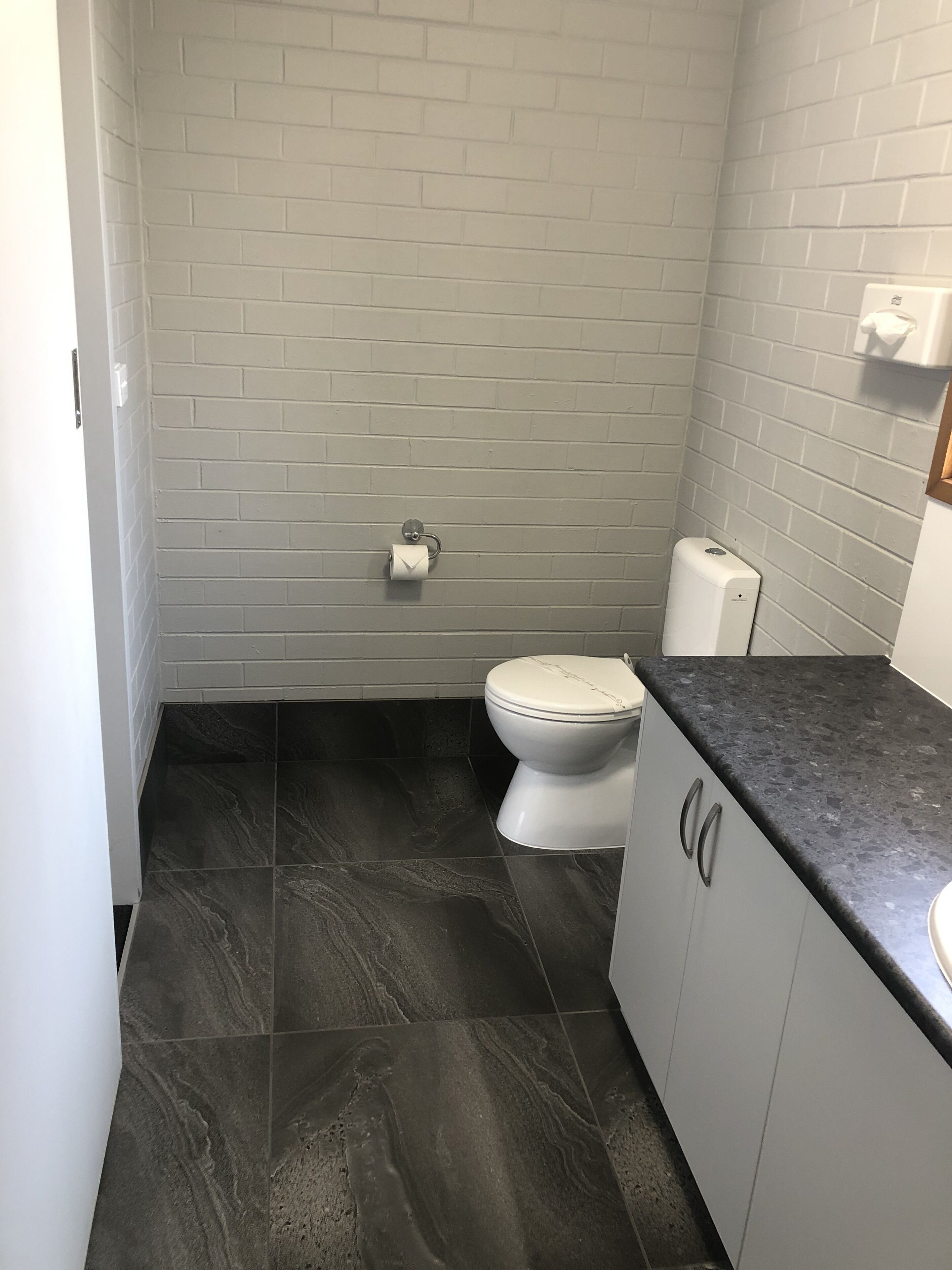 A small bathroom with a toilet, a paper towel dispenser, and a soap dispenser.