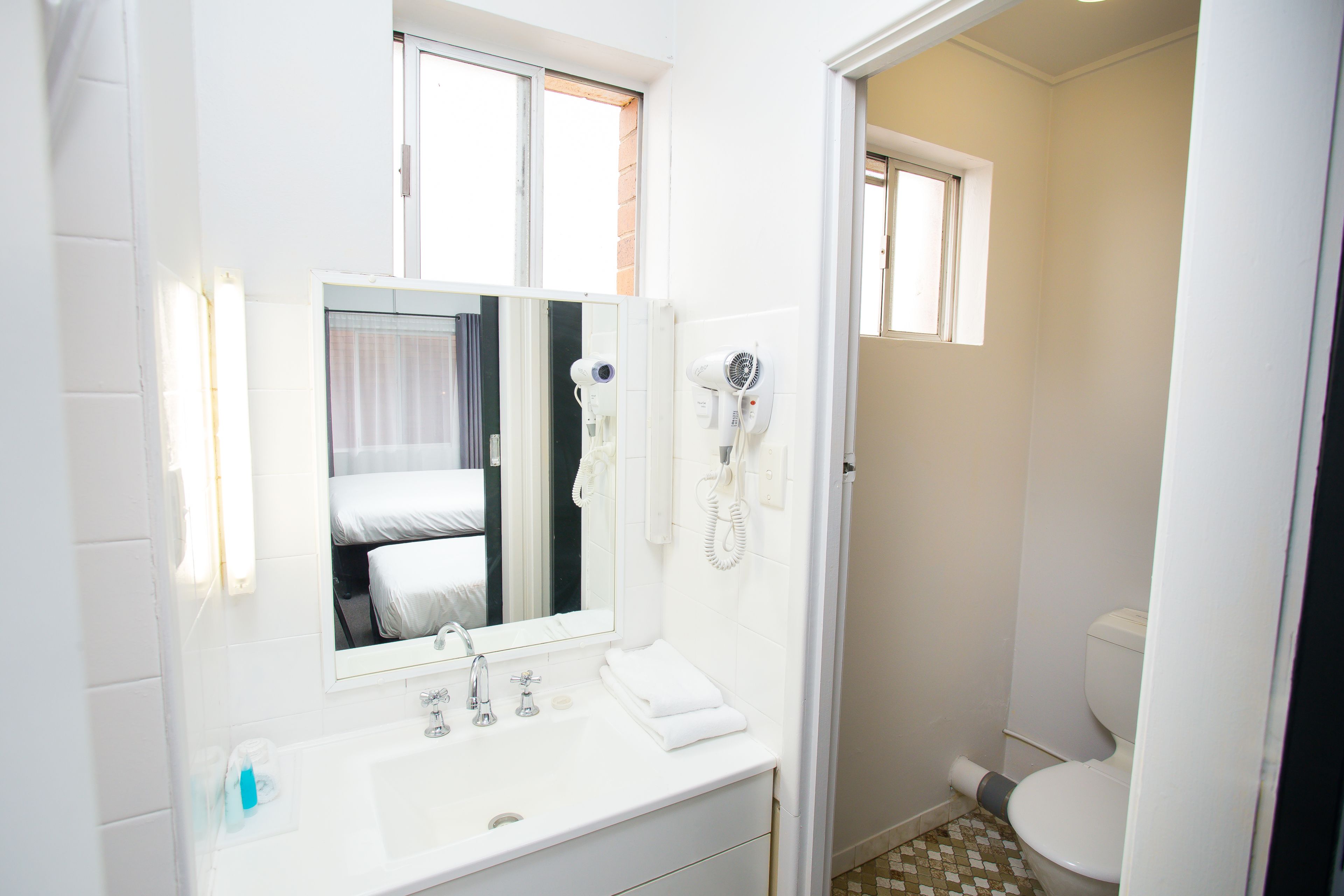 A bathroom with a white sink, mirror, and two hair dryers mounted on the wall.