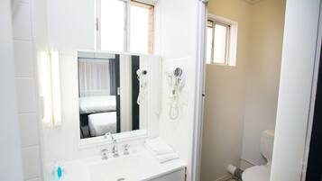 Ein Badezimmer mit einem weißen Waschbecken, einem Spiegel und zwei Haartrocknern, die an der Wand angebracht sind.