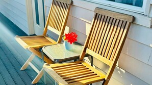 Two wooden chairs with slatted seats and backs, a small table with a vase of red flowers, and a window with white shutters. - Downs Motel (South Toowoomba)