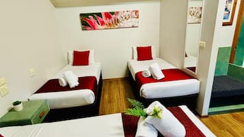 A hotel room with two beds, each with red and white bedding, a small table with a plant, and a mirror on the wall.