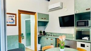 A compact kitchen with a microwave, stove, and sink. There is a dining area with a table and chairs, and a small seating area with a bench. - Downs Motel (South Toowoomba)
