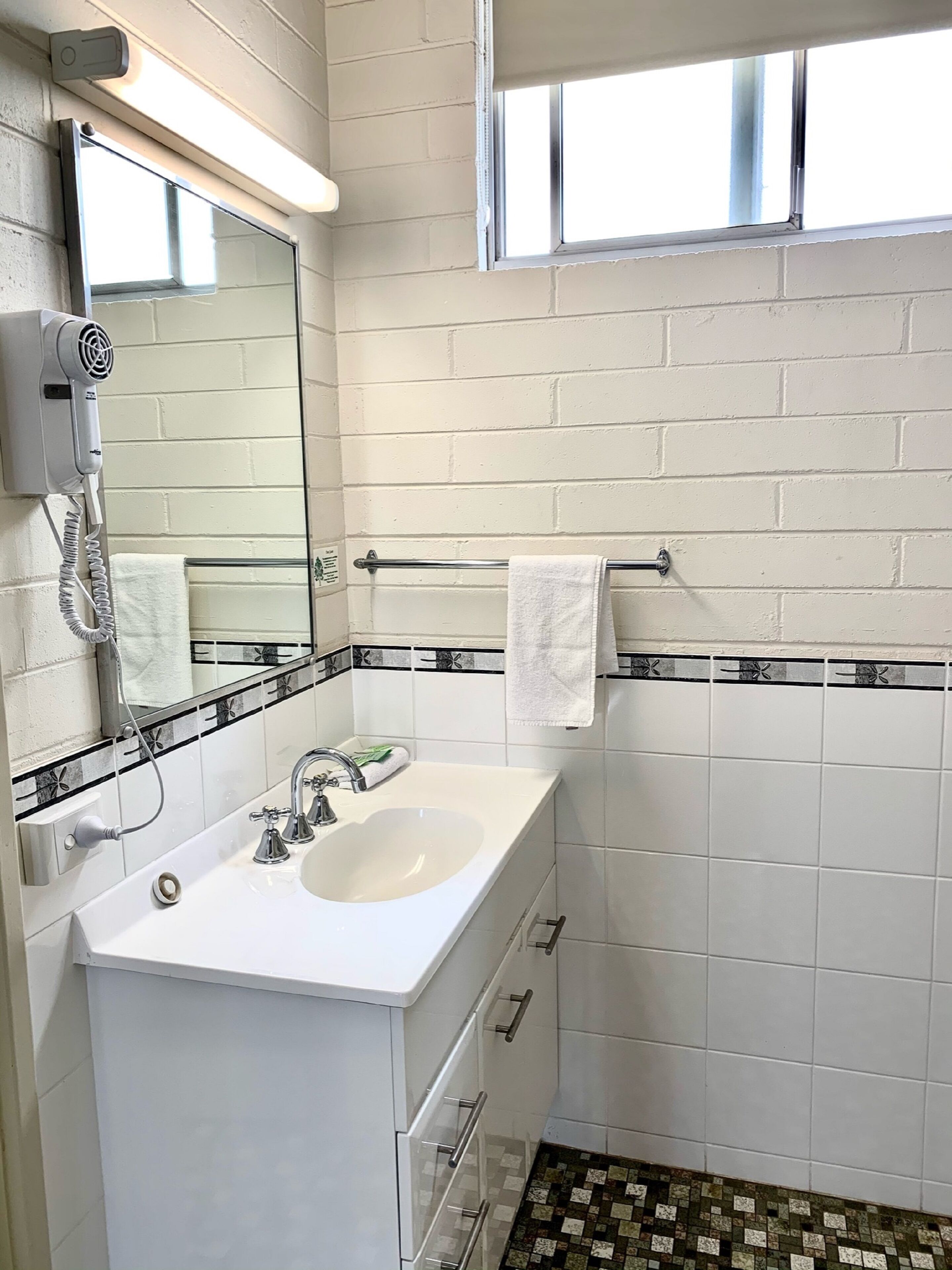 Une salle de bain avec un lavabo blanc, un miroir, un porte-serviettes et une fenêtre.