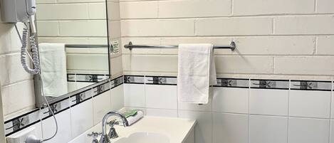 Un bagno con un lavandino bianco, uno specchio, un portasciugamani e una finestra.