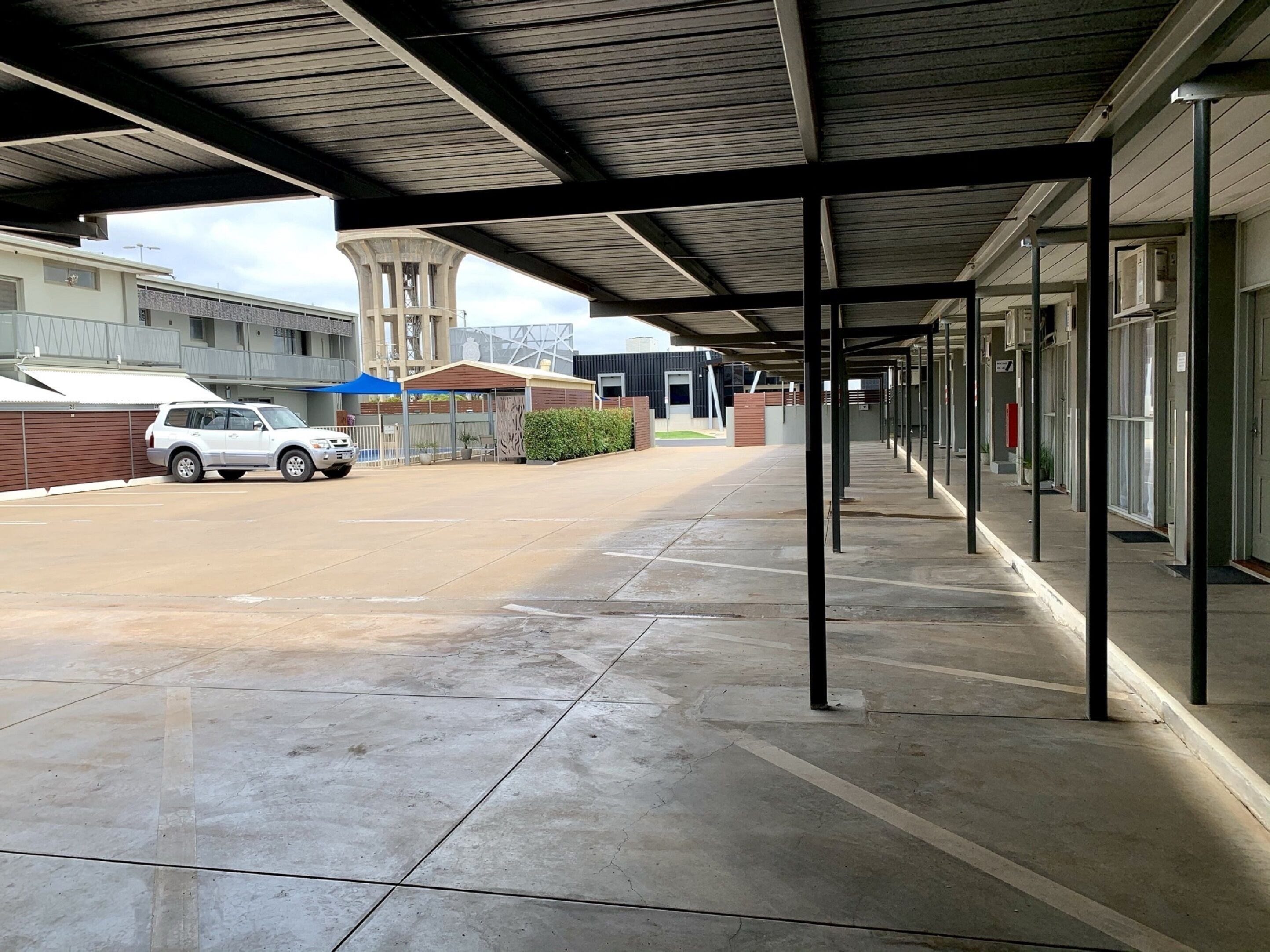 A covered parking area with a white SUV parked, a building with a modern design, and a clear sky.
