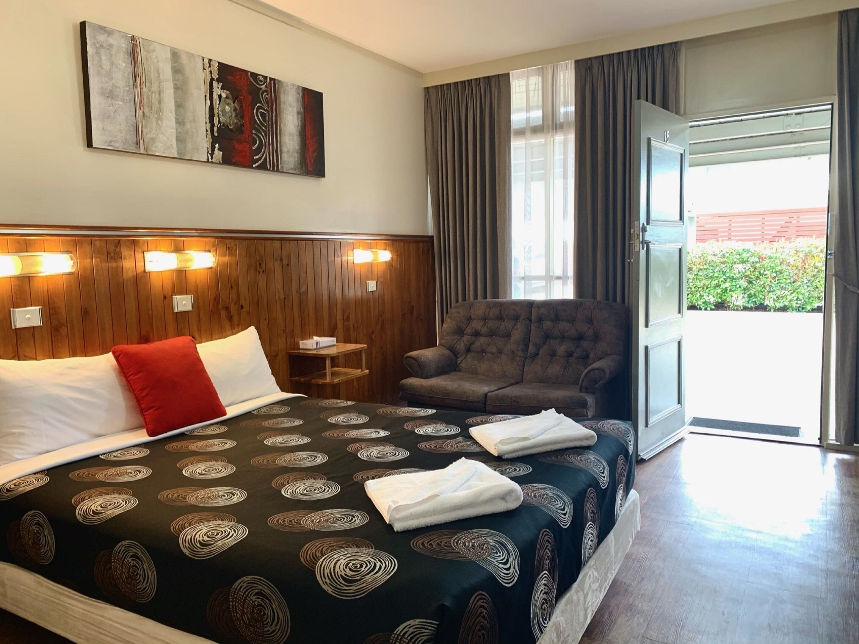 A hotel room with a large bed, a seating area, and a view of the outdoors.